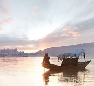 Boat man paddles traditional boat (shikara) in Lake Pichola at sunrise.